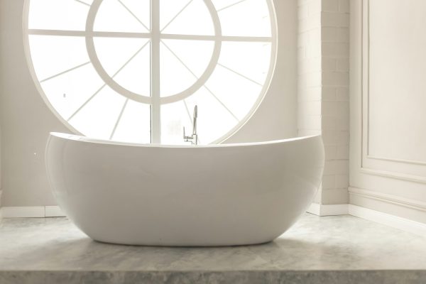 White modern floor bathtub with round window and pastel painted walls with stucco